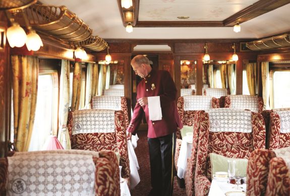 a train steward in traditional smart uniform checking the tables on a vintage style northern belle train carriage