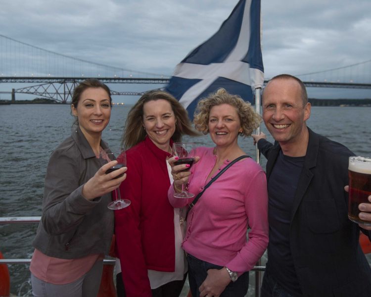 four people posing for a photo on the deck of a cruise boat on an evening themed sightseeing cruise in scotland