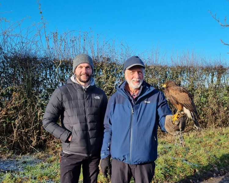 2 men standing together one holding a falcon
