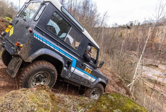 a black land rover off road vehicle driving down a muddy slope on a driving course in gloucestershire