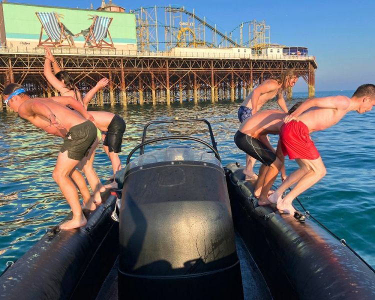 Group of people jumping off a speedboat into the sea