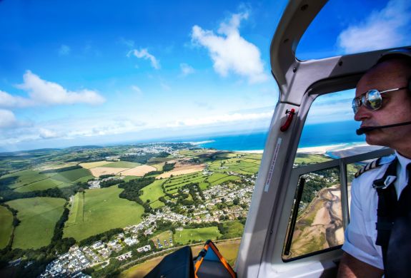 photo taken in the cockpit of a helicopter showing the pilot and the views below of the coastline