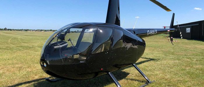 a black helicopter on grass against a blue sky as part of a helicopter flying lesson