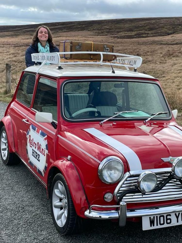 a woman standing behind a classic red mini cooper on a self drive road trip