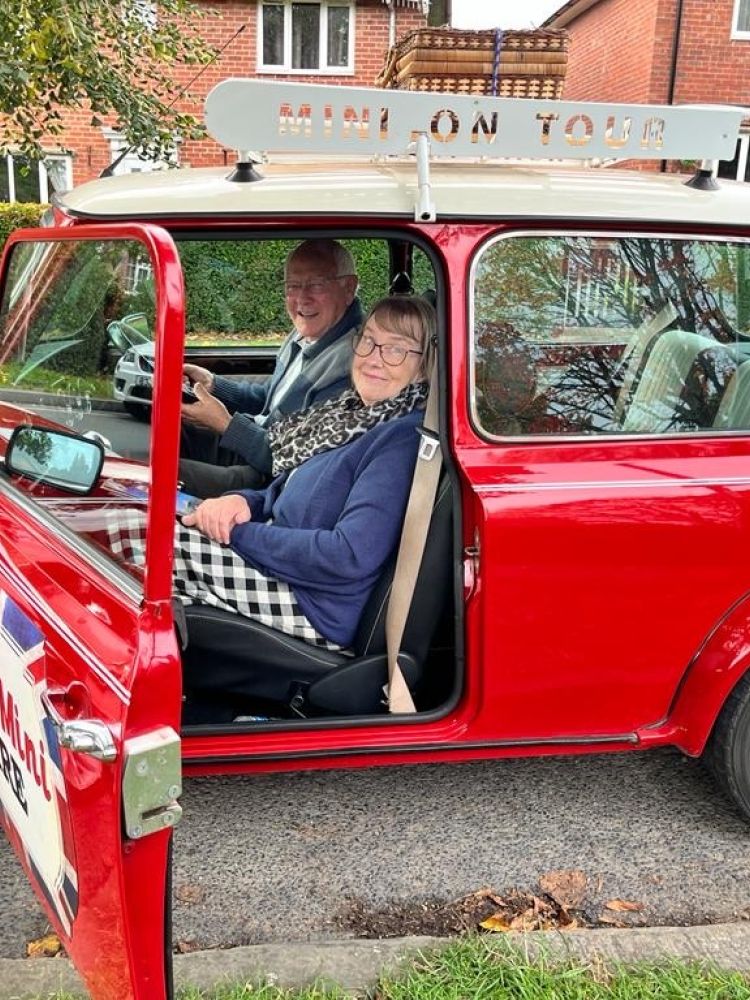 a man and a woman sitting inside a classic red mini cooper ready to go on a self drive road trip