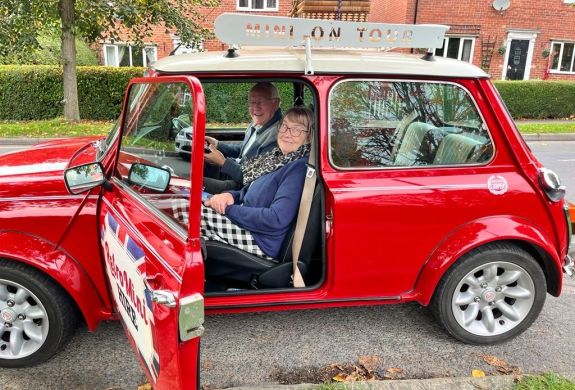 a man and a woman sitting inside a classic red mini cooper ready to go on a self drive road trip