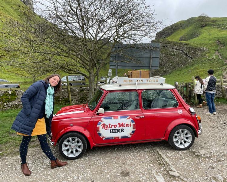 a woman standing alongside a classic red mini cooper on a self drive road trip