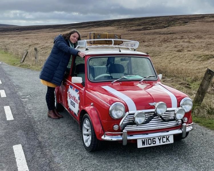 a woman standing alongside of a classic red mini cooper on a self drive road trip
