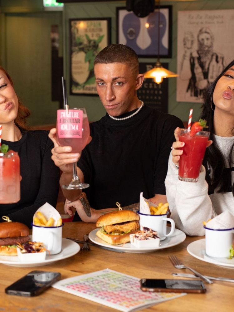 3 guests posing with cocktails and burgers