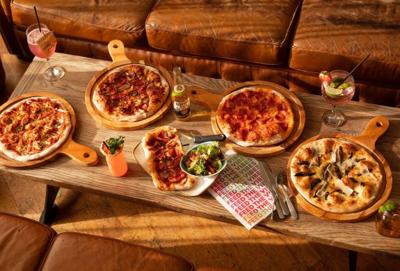 an assortment of 4 pizzas on a coffee table