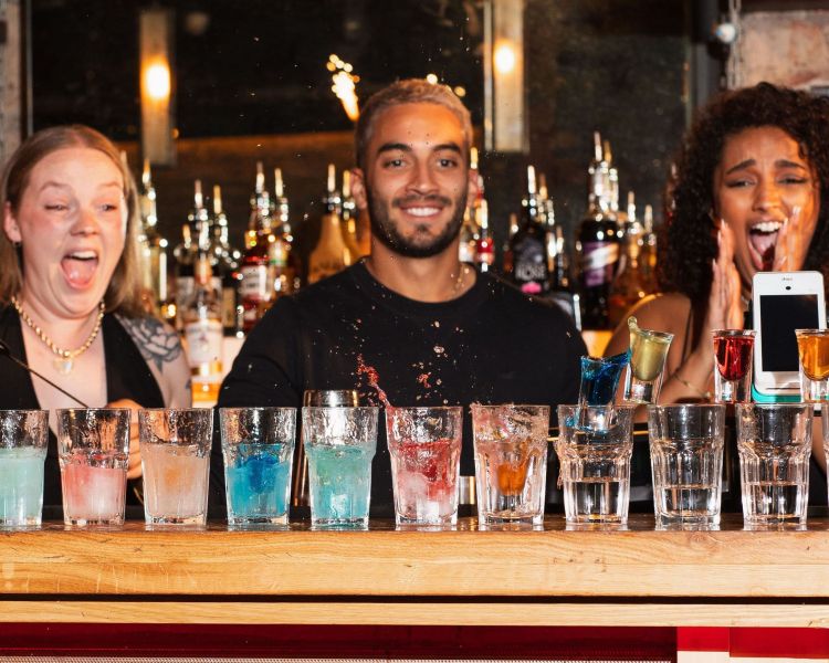 3 bartenders looking at a line of cocktails with excitement