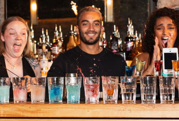 3 bartenders looking at a line of cocktails with excitement