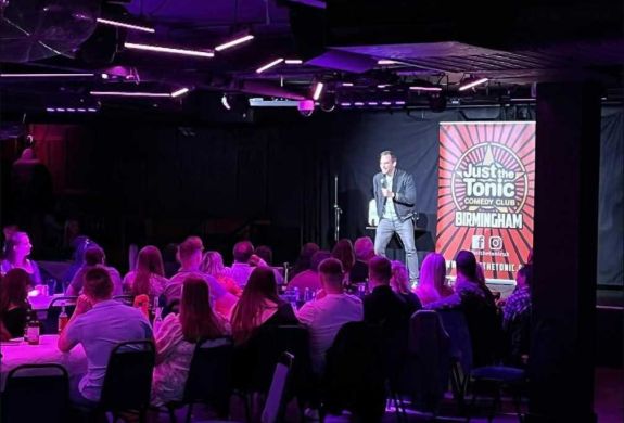 a comedian on stage with people looking on at a comedy night