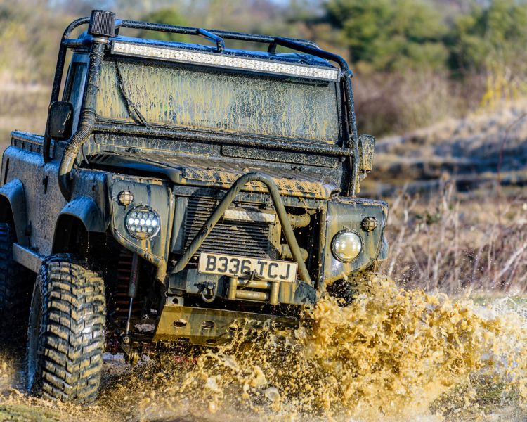 a mad max inspired land rover driving off road through a muddy puddle on a driving experience day