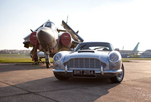 a british classic car next to an airplane on an airfield track