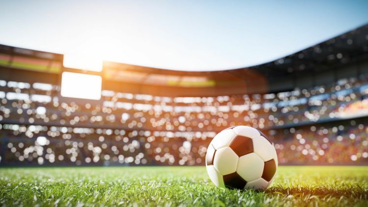 A black and white football on a football pitch inside a stadium