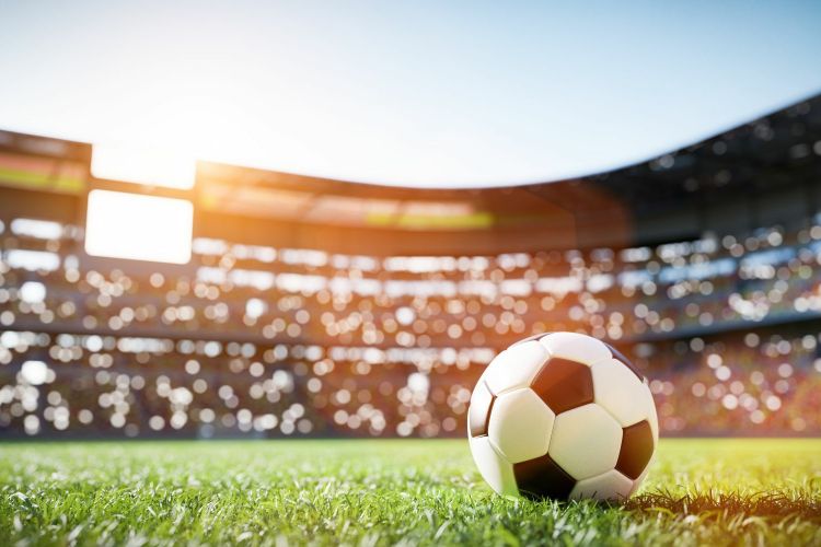 A black and white football on a football pitch inside a stadium