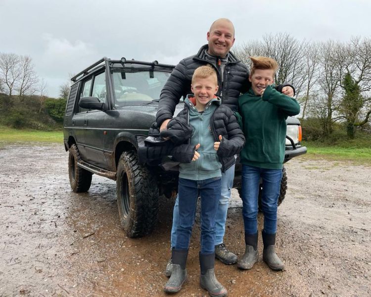 a man and two young boys standing in front of a 4 x 4 vehicle as part of a driving experience