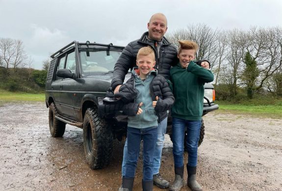 a man and two young boys standing in front of a 4 x 4 vehicle as part of a driving experience