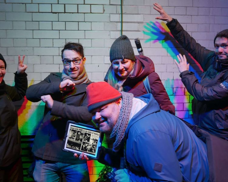 four people posing with a tour guide in front of a white tiled wall on the beatles walking tour in london