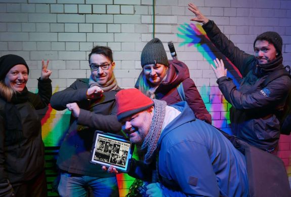 four people posing with a tour guide in front of a white tiled wall on the beatles walking tour in london