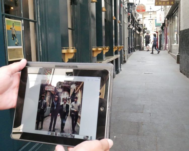hands holding a photo of the beatles in the same alleyway where the photo was taken seen on the beatles walking tour