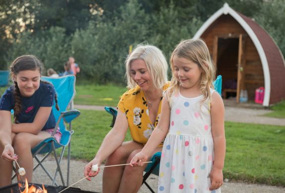 Family time toasting marshmallow in campfire camping pod holiday