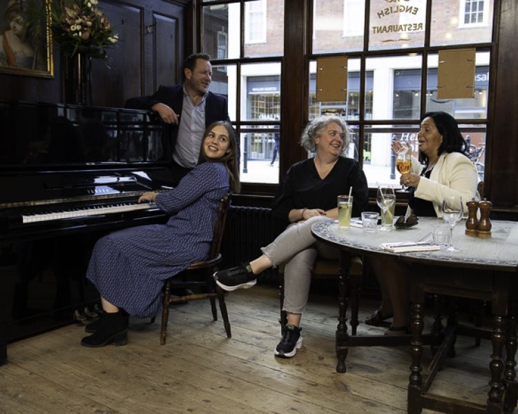 people enjoying a drink in a pub with one of them sitting at a piano