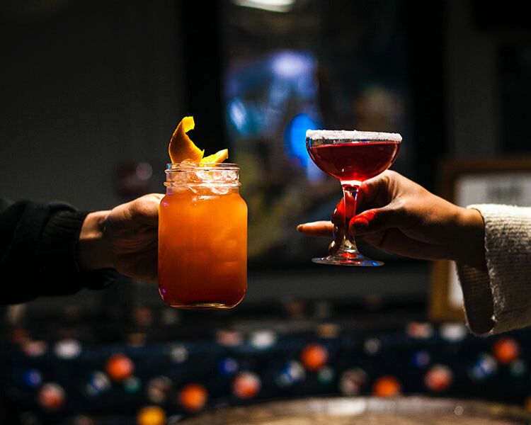 a shot of two arms each holding a different cocktail
