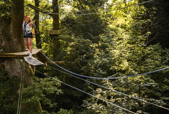 woman about to cross an obstacle on the zip world full trek manchester treetop obstacle course