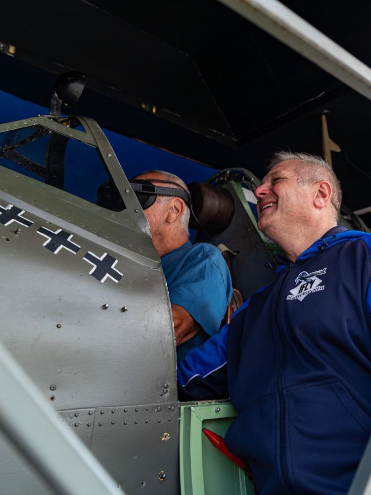 man in a spitfire flight simulator with another man looking on