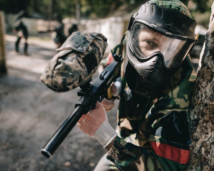 young man dressed in camouflage gear holding a paintball gun on a paintball experience