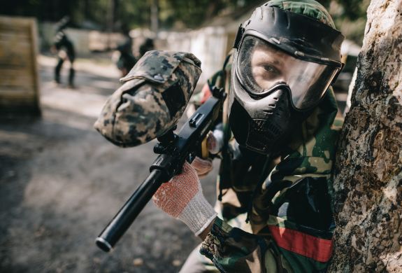 young man dressed in camouflage gear holding a paintball gun on a paintball experience