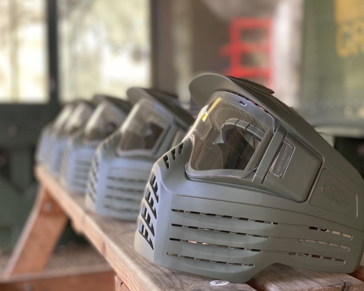 a row of paintball helmets on a wooden shelf for a paintball experience