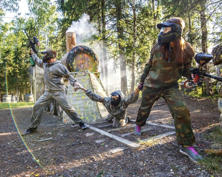 two people pulling a person up off the ground while on a paintball experience