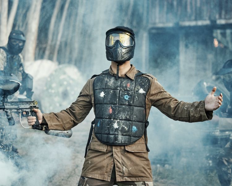 young man with paint splatters on his chest holding a paintball gun on a paintball experience