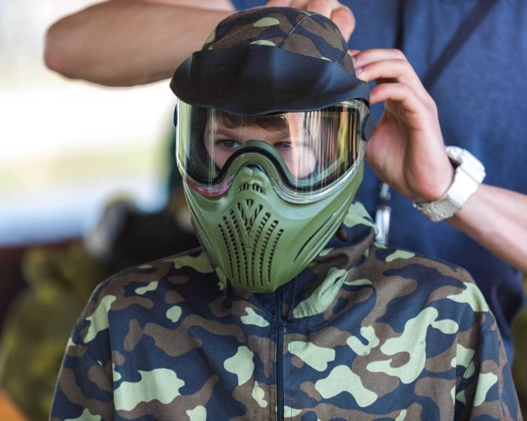 a young boy being fitted with a paintball mask ready for a paintball experience