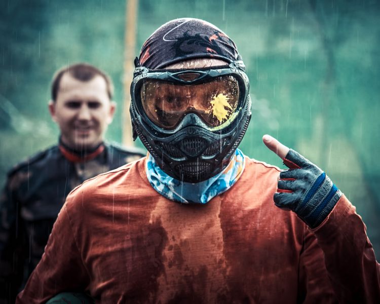 man in full paintball gear pointing to a paint splatter on his helmet