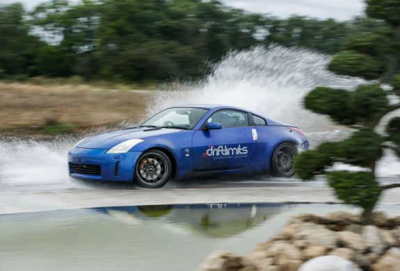 a blue sportscar driving through water on a track as part of a nissan and bmw drift battle experience day