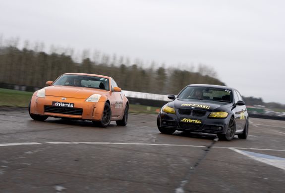 an orange sportscar and a black sportscar side by side on a race track as part of a drift battle nissan 350z driving experience day