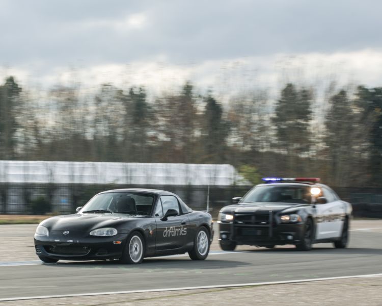 black sports car being chased by a police car on a race track as part of a police pursuit experience