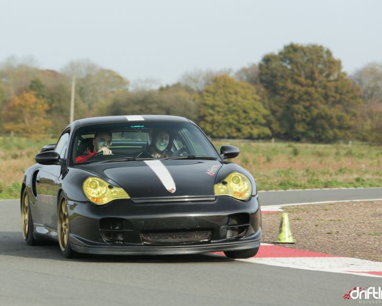 a black supercar being driven around a bend of a race course with an instructor sat next to the driver