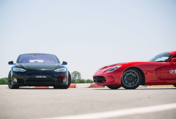 two supercars, a tesla and a viper, side by side on a race track.