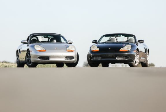 front view of a silver porsche boxter next to a black porche boxter on a track
