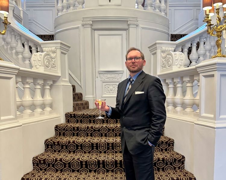 man wearing smart suit holding a martini in front of a grand staircase as part of james bond tour