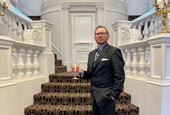 man wearing smart suit holding a martini in front of a grand staircase as part of james bond tour