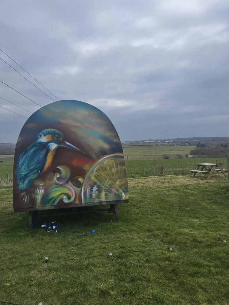 a glamping pod painted with a kingfisher on the back overlooking countryside for a stonehenge unique stay