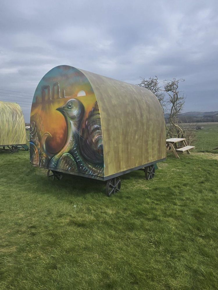 a glamping pod painted with a bird and stonehenge on the back overlooking countryside for a stonehenge unique stay