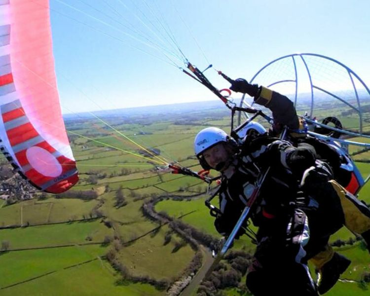 man on a tandem paramotor experience flying over green fields against blue skies