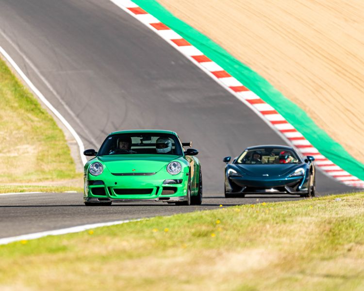 a green supercar followed by a black supercar on a race track for a driving experience